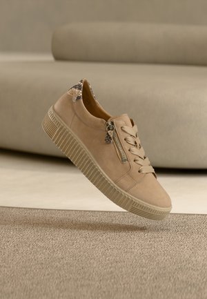 Beiger Wildledersneaker mit strukturierter Gummisohle, Schnürdesign, seitlichem Reißverschluss und gemusterten Akzenten an der Ferse.