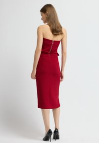 Rode jurk met een aansluitend ontwerp, strapless, met een rits aan de achterkant en een knielange silhoutte. Gepaard met zwarte hoge hakken.