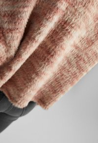 Miękki sweter w różowym odcieniu o puszystej fakturze, z luźnym krojem i wzorzystym motywem, opadający na ciemnoszare dżinsy.