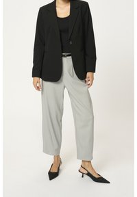 Blazer nero su misura con rever a notched, pantaloni grigi a gamba larga e décolleté slingback neri con punta affusolata. Tessuto liscio e strutturato.