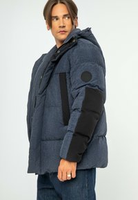 Námořnická prošívaná bunda s kostkovaným vzorem, černými akcenty, zipem a druky, nastavovací kapucí a kulatou nášivkou loga na rukávu.