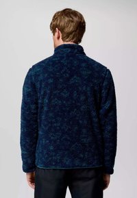 Giacca in pile blu navy con colletto alto, tessuto testurizzato e motivo sottile. Presenta maniche lunghe e un orlo dritto nella parte inferiore.