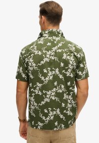 Groene shirt met korte mouwen, voorzien van een wit bloemenpatroon, gemaakt van gestructureerde stof, met een klassieke kraag en een rugpasdetail.