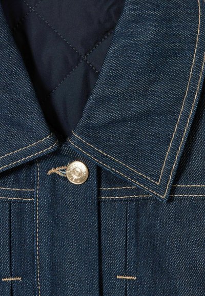 Cuello de chaqueta de denim azul oscuro con costuras en beige contrastantes y un botón plateado abrochado en la parte superior.