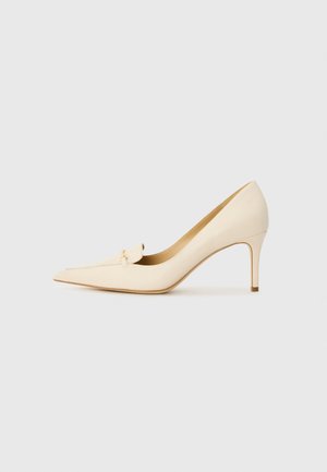 Escarpin beige à bout pointu, en cuir lisse, avec un petit accent décoratif à l'avant. Talon de 7,5 cm.