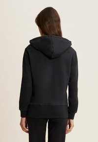 Sudadera negra con una textura suave, mangas largas y una capucha con cordón ajustable. Los puños y el dobladillo acanalados realzan el diseño.