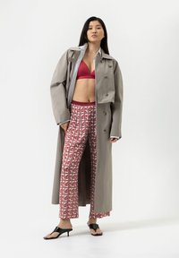 Manteau long gris avec de grands boutons, soutien-gorge rouge et pantalon large à motifs avec des pois rouges et roses. Des sandales noires complètent le look.