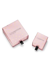 Dos cajas de regalo rosas con lunares dorados; la caja más grande tiene un logo y una cinta de tiro negra, mientras que la caja más pequeña presenta el mismo diseño.