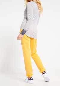 Pruhované dlouhé tričko s oblým lemem v kombinaci se žlutými tepláky. Oblečení má kontrastní manžety na rukávech a bílé tenisky.