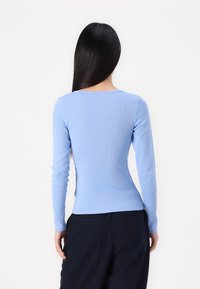 Lyseblå ribbestrikket langermet topp med rund hals, tettsittende design og glatt tekstur, kombinert med mørkfargede bukser.