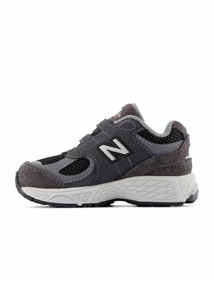 Chaussure de sport grise en matériaux mesh et suède, offrant une semelle moulée, une sangle ajustable et un logo 'N' bien visible sur le côté.