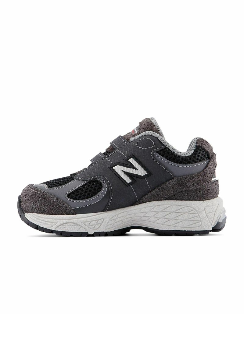 Chaussure de sport grise en matériaux mesh et suède, offrant une semelle moulée, une sangle ajustable et un logo 'N' bien visible sur le côté.