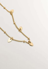 Collar de cadena de oro con colgantes en forma de lágrima, cuentas redondas y un diseño retorcido. Textura suave con superficies brillantes y reflectantes.
