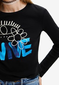 Schwarzes, geripptes Langarmshirt mit weißen, gestickten Augen- und Blumendesigns. Mit blauem und lila Pinselstrich-Text, der "VIVE" spell.