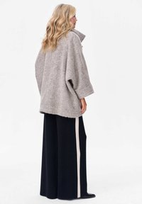 Lichtgrijze oversized jas met een textuurafwerking, opgerolde mouwen en een hoge kraag, gecombineerd met zwarte wijde broek met een beige streep.