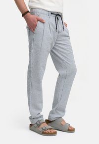Stribede bukser i en blanding af hør med elastisk talje, frontfoldninger og sidelommer, i nuancer af blå og hvid; parret med grå sandaler.
