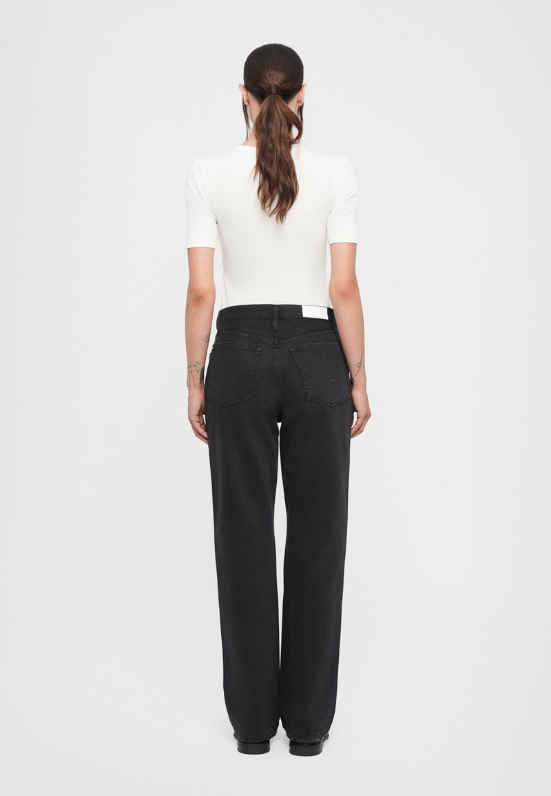 Jean large noir à taille haute, doté de deux poches arrière et d'une étiquette blanche contrastante. Accompagné d'un haut blanc ajusté.