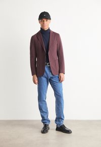 Bordowy żakiet, granatowy golf, niebieskie dżinsy, czarne buty i czapka. Gładki materiał, dopasowany krój i minimalistyczny design.