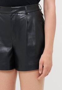 Svarta lädershorts med en mjuk textur, med hög midja, skarpa veck framtill och en åtsittande silhuett.