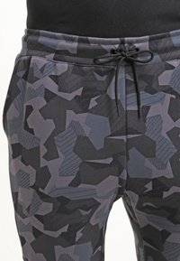 Svarta och grå mönstrade joggers med dragsko i midjan, geometriska mönster och en mjuk tygtextur.