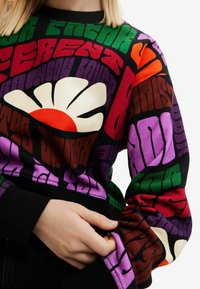 Farverig sweatshirt med fed tekst og en stor hvid blomst med orange midte. Lavet af blødt stof med ribstrikkede manchetter.