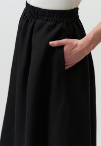Zwarte rok van textuurstof, met een elastische tailleband en zijzakken, met een losse, vloeiende pasvorm.
