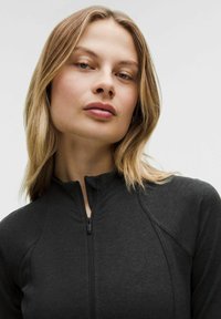 Schwarze Jacke mit Reißverschluss, hohem Kragen und strukturiertem Stoff. Mit Raglanärmeln und einem glatten Reißverschlussakzent.