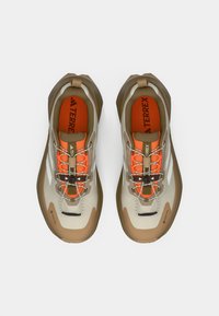 Ελαφριά παπούτσια για υπαίθρια χρήση με μπεζ και καφέ σχέδιο, πορτοκαλί αποχρώσεις, υφή στην επάνω επιφάνεια και αντανακλαστικά κορδόνια. Διακρίνεται η επωνυμία Gore-Tex.