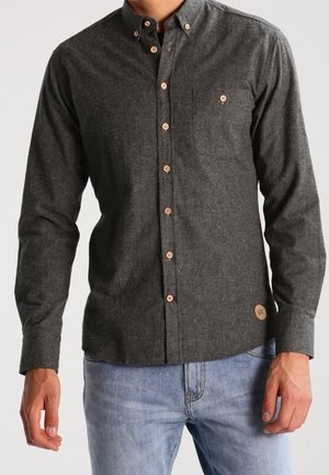Camisa de manga larga gris oscuro con botones color beige, bolsillo en el pecho, usada con vaqueros azul claro.