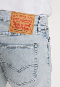 Ljust blå denimjeans med en brun läderpatch som visar "LEVI STRAUSS & CO." logotyp, med information om patentdatum och stil.