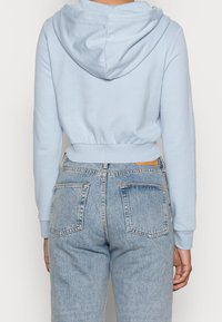 Sudadera recortada azul claro con capucha ajustable, dobladillo elástico y mangas largas, combinada con jeans de mezclilla azul claro de talle alto.