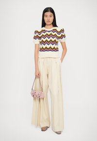 Pull en tricot avec un motif en zigzag multicolore, manches courtes bouffantes, de couleur crème, associé à un pantalon crème taille haute et un petit sac rose.