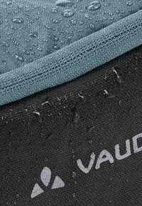 Sac résistant à l'eau présentant une base noire texturée avec un dessus texturé gris. La surface montre des gouttes, indiquant un matériau imperméable.