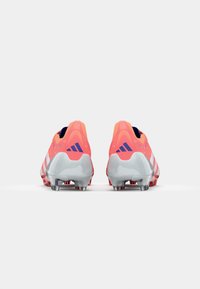 Scarpette da calcio rosa brillante con dettagli argento, design a taglio basso e tacchetti evidenti. Presentano il logo del marchio sul tallone e una parte superiore con motivo.