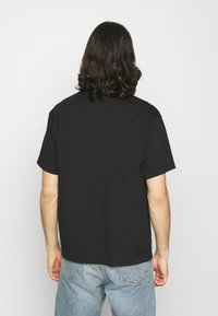 Černé tričko s krátkým rukávem, volného střihu a kulatým výstřihem, vyrobené z bavlněné tkaniny, pohled zezadu.