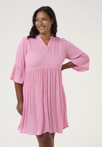 Robe rose, longueur genou, avec un décolleté en V et des manches 3/4 évasées. Tissu texturé, taille froncée et jupe ample.
