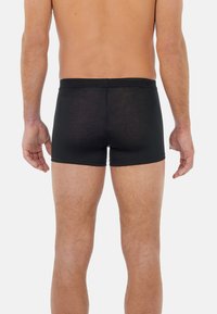 Svarta boxershorts tillverkade av mjukt tyg, med elastisk midja, åtsittande passform och en minimalistisk design. Bakvy.