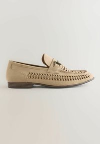 Mocassin en daim beige avec détails tissés sur les côtés, boucle décorative en métal et petit talon en bois empilé.
