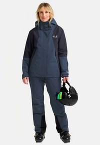 Donkerblauw ski-jas en broek met zwarte accenten. Waterdichte stof, hoge kraag en verstelbare manchetten. Bevat een skihelm met reflecterend vizier.