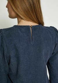 Navyblaues, strukturiertes Kleid aus geripptem Stoff, mit einer Rückenöffnung in Form eines Schlüssellochs, die durch einen runden Knopf gesichert ist. Lange Puffärmel sind vorhanden.