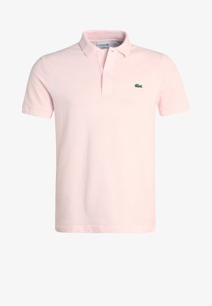 Pikétröja i ljusrosa bomull med klassisk krage, två knappar och en liten grön krokodil-logotyp på vänster bröst. Korta ärmar.