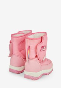 Botas de invierno aisladas de color rosa con un exterior suave, forro blanco suave y cierre ajustable de Velcro. Presentan un parche con el logo y suela texturizada.
