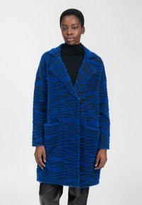 Abrigo fuzzy a rayas en azul y negro, con cuello, dos bolsillos frontales y mangas largas, que presenta un corte holgado y una textura suave.