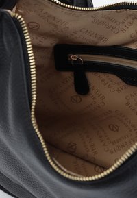 Sort læderhåndtaske med en tekstureret overflade og en gylden lynlås. Foringen har et beige mønster med "CAFÉ NOIR" branding.