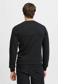 Felpa nera con maniche lunghe e scollatura rotonda; texture liscia e polsini e orlo a coste; indossata con pantaloni scuri.