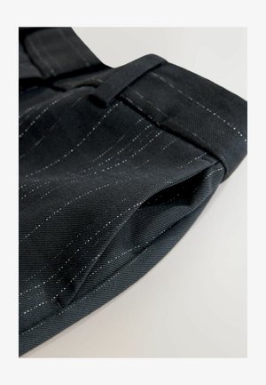 Sorte bukser i stof med et subtilt indgående mønster i hvidt, med et nærbillede, der fremhæver tekstur og sømdetaljer.