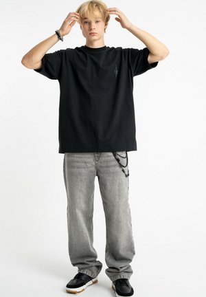 Czarny bawełniany oversize t-shirt z małym logo, zestawiony z jasnoszarymi luźnymi dżinsami z łańcuchami oraz czarnymi sneakersami.