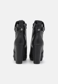 Botines negros de tacón alto fabricados en cuero, con cierre de cremallera, detalles de hebilla y un tacón grueso y cuadrado. Acabado suave y mate.