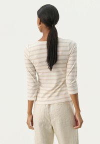 Beige stribet langærmet top med en scoop-ryg halsudskæring, parret med lysebeige linnedbukser. Glat tekstur, tætsiddende stil og afslappet design.