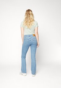 Siniset leveät farkut, joissa on keskikorkea vyötärö ja takataskut. Yhdistetty vihreäraitaisen t-paidan kanssa. Vaalea denim, jossa on nahkainen logo-vetoketju.